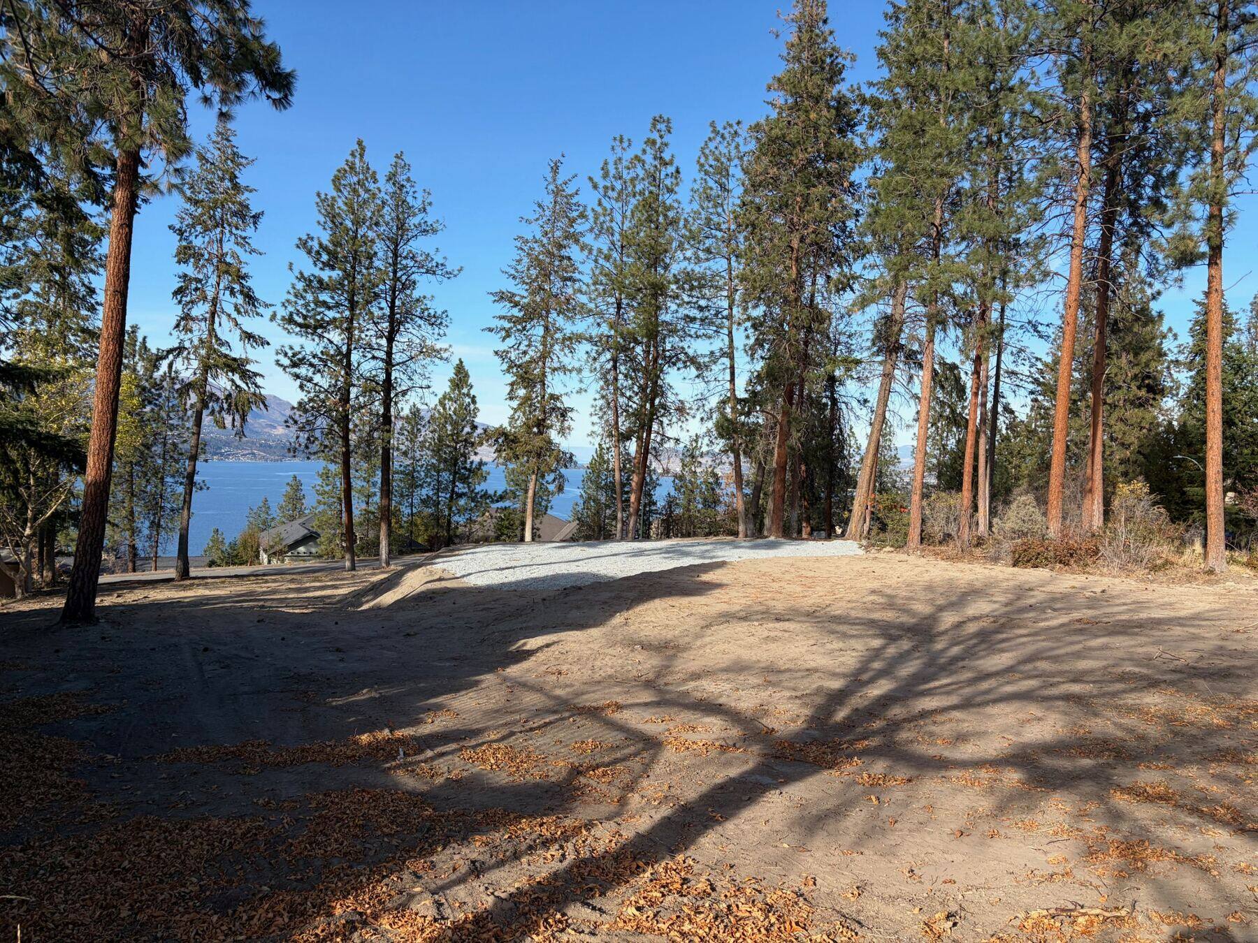 Wide view from the lot across the gravel building pad to Okanagan Lake and the mountains