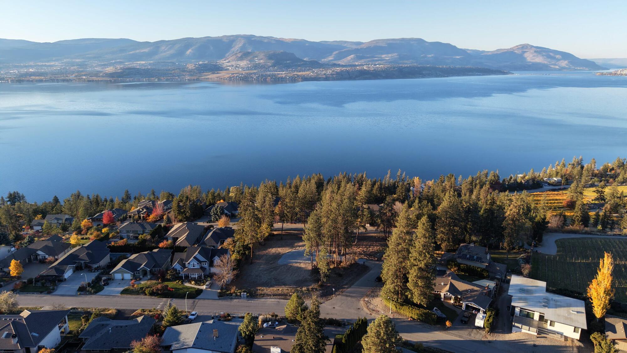 Aerial view of the cleared lot among tall ponderosa pines in the Upper Mission, with Okanagan Lake and the mountains beyond